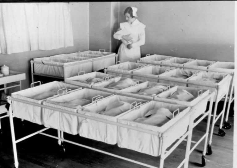 Nurse presides over racks of infants in the nursery.