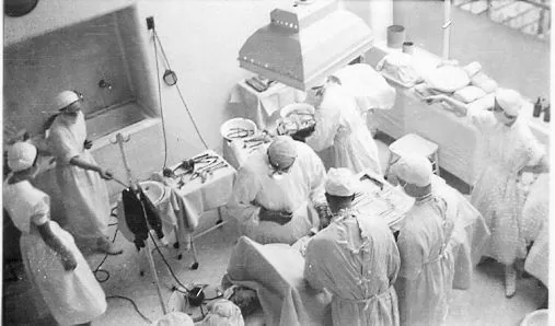 Many nurses and attendants surround surgeons working on patient.