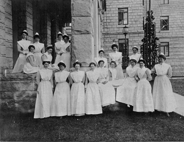 A group of nurses in uniform gather on the lawn of the Heather Pavilion.