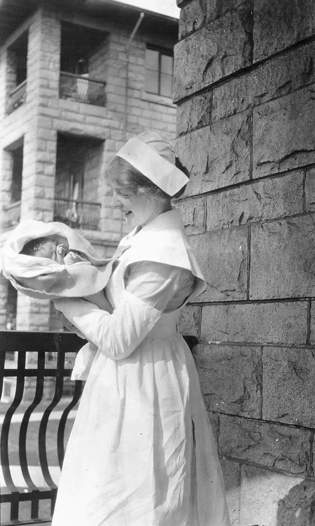 Nurse "Doll" Sharp holds an infant on a patio of the Heather Pavilion.