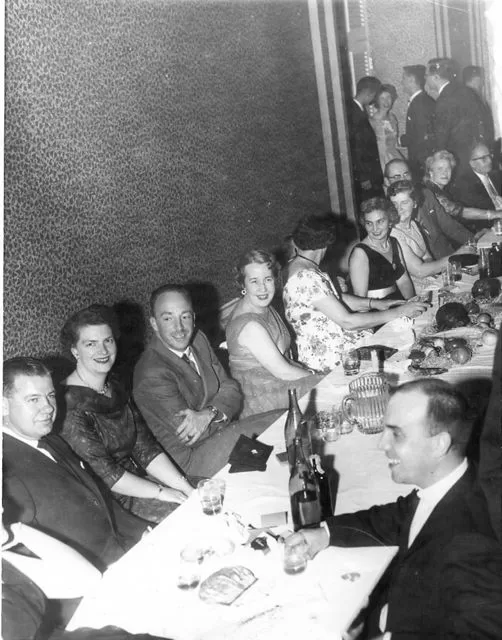 Faculty members, both male and female, gathered around a long banquet table at the Students' Broad Bib Dance in 1960.