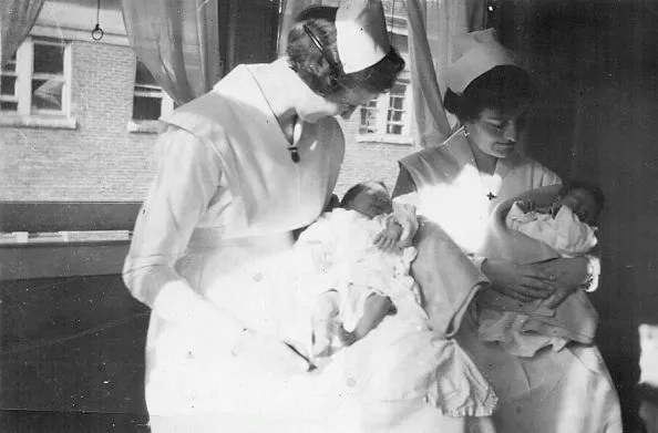 Miss Tretheway and Olive Diamond wear nursing uniforms and sit holding two infants.