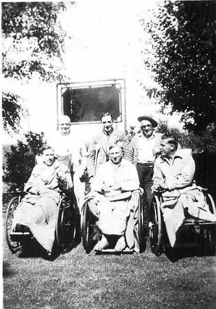 Six male patients outside, three seated in wheelchairs and one standing on crutches, posing on the hospital lawn.