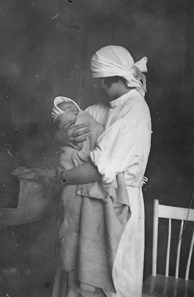 Nurse wearing a sterile cap holds a swaddled infant.