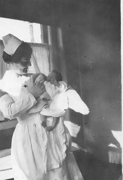 Nurse Olive Diamond holding an infant and bottle feeding them.