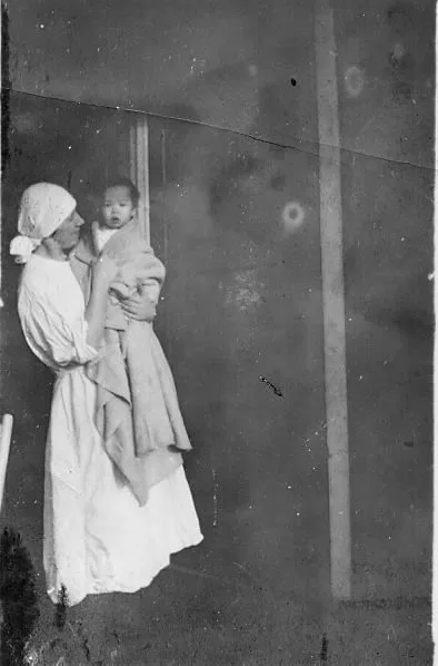 A nurse wearing a sterile cap holds an infant swaddled in a blanket.